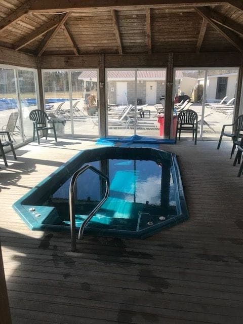 Enclosed hot tub with wooden deck and seating area overlooking the pool