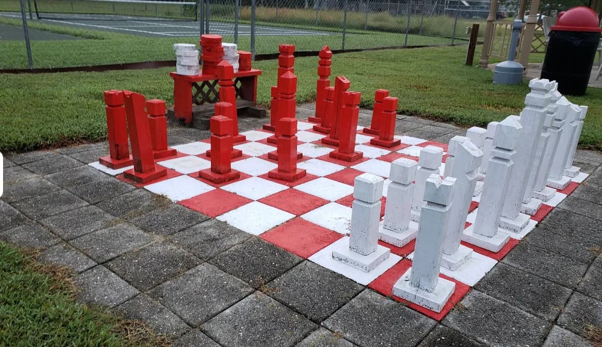 Life-sized outdoor chess set with red and white pieces on patio