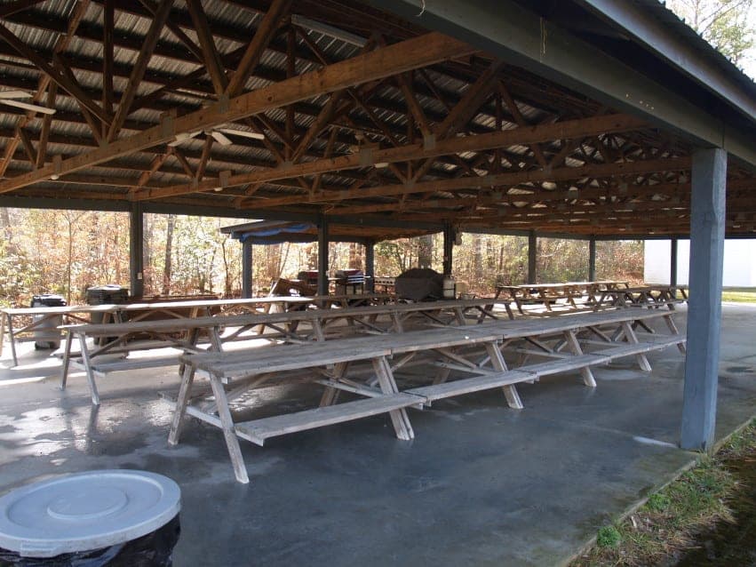 Covered outdoor pavilion with wooden picnic tables and BBQ grills